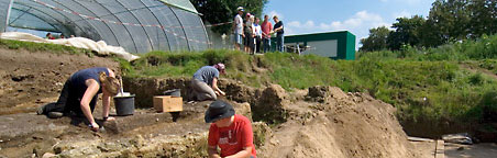 Unter den Augen einer geführten Besuchergruppe arbeitet ein Ausgrabungsteam zwischen römischen Grundmauern.
