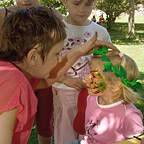 Het gezicht van een jong meisje met een papieren lauwerkrans in het haar wordt kleurrijk geschminkt. 