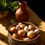 Basket with onions and garlic, a jug and fresh herbs on a wooden table.