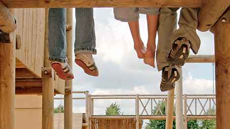 Three children dangle their legs from a climbing frame on the playground of the park.