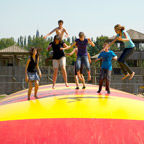 Youths jumping on a big, colourful bouncy pillow.