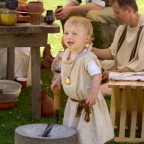 Ein kleiner Junge in römischer Kleidung arbeitet an einem großen Mahlstein.