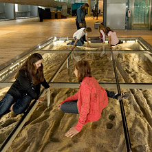 Een groepje kinderen zit op een glazen vloer waaronder Romeinse voetafdrukken te zien zijn. 