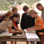 Eine Gruppe Studierender diskutiert die Ergebnisse ihrer Arbeit über einem Ordner mit den Grabungszeichnungen.