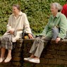 Zwei Seniorinnen sitzen auf einer Mauer im Park.