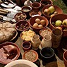 Talrijke schotels, kannen en bekers staan op tafel; alle gevuld met verschillende levensmiddelen.