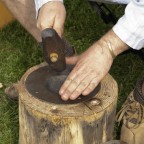 Die Hände eines Schmiedes bei Treibarbeiten auf einem Holzblock.