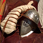 Close-up of a gladiator's equipment including a helmet and a padded arm-guard.