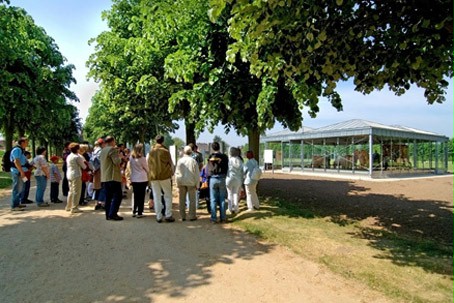 Eine Besuchergruppe steht auf einer Allee und blickt auf den gläsernen Themen-Pavillon zum Thema Reisen und Verkehr.