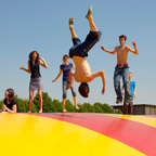 Youths jumping on a big, colourful bouncy pillow.