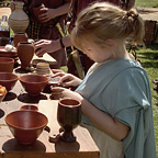 A young girl in a light blue Roman dress is looking at Roman pots.