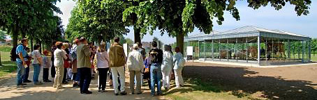 Eine Besuchergruppe steht auf einer Allee und blickt auf den gläsernen Pavillon zum Thema Reisen und Verkehr.