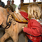 A girl touches the wooden model of a horse in the themed pavilion „Travel & traffic“.