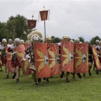 Mehrere römische Legionäre stellen sich hinter ihren Schutzschulden auf.