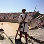 Ein Mann in römischer Kleidung blickt in das mit vielen Zuschauern gefüllte Amphitheater.