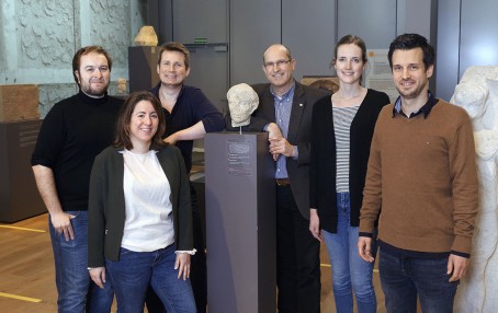 Das Museumsteam steht um einen Sockel mit römischem Statuenkopf im Museum
