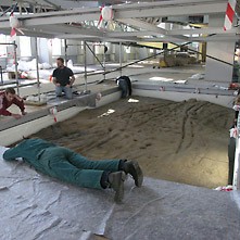 Mehrere Personen präparieren für die Ausstellung im RömerMuseum eine Fläche, auf der sich römerzeitliche Laufspuren erhalten haben.