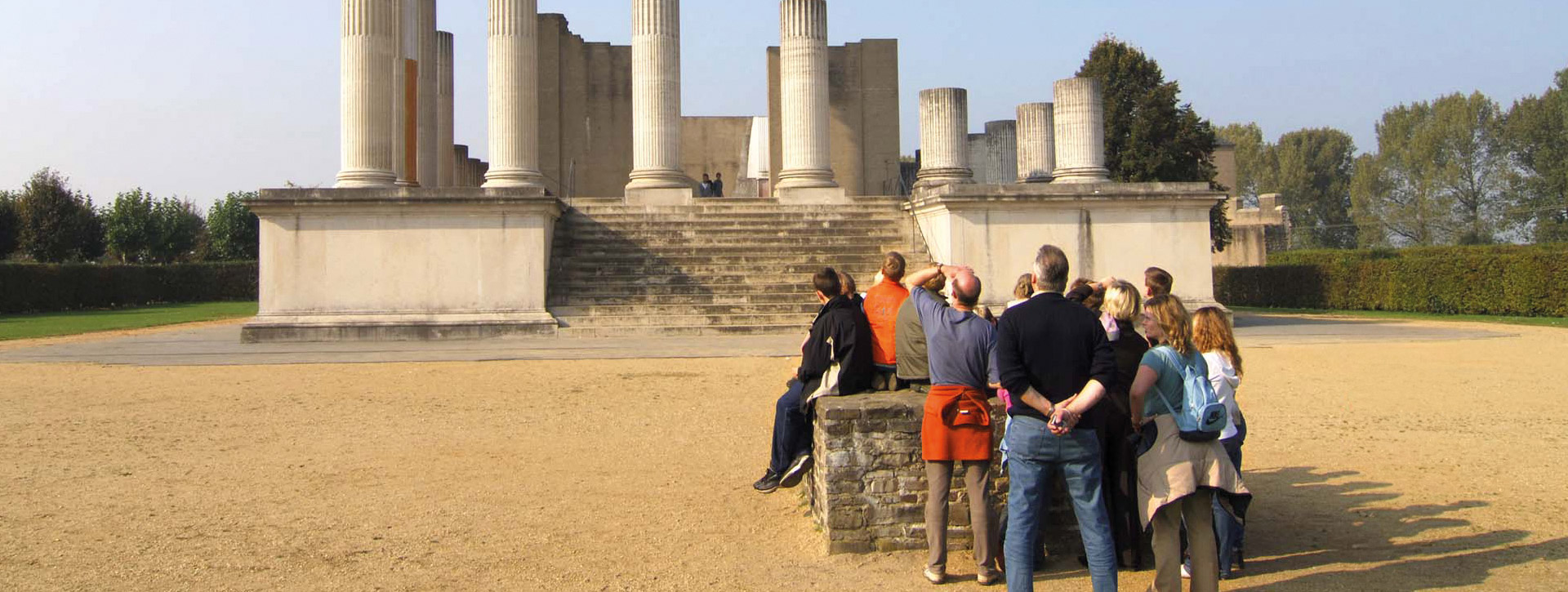 Gruppe von etwa einem Dutzend Menschen vor dem teilrekonstruierten Hafentempel, Rücken zur Kamera