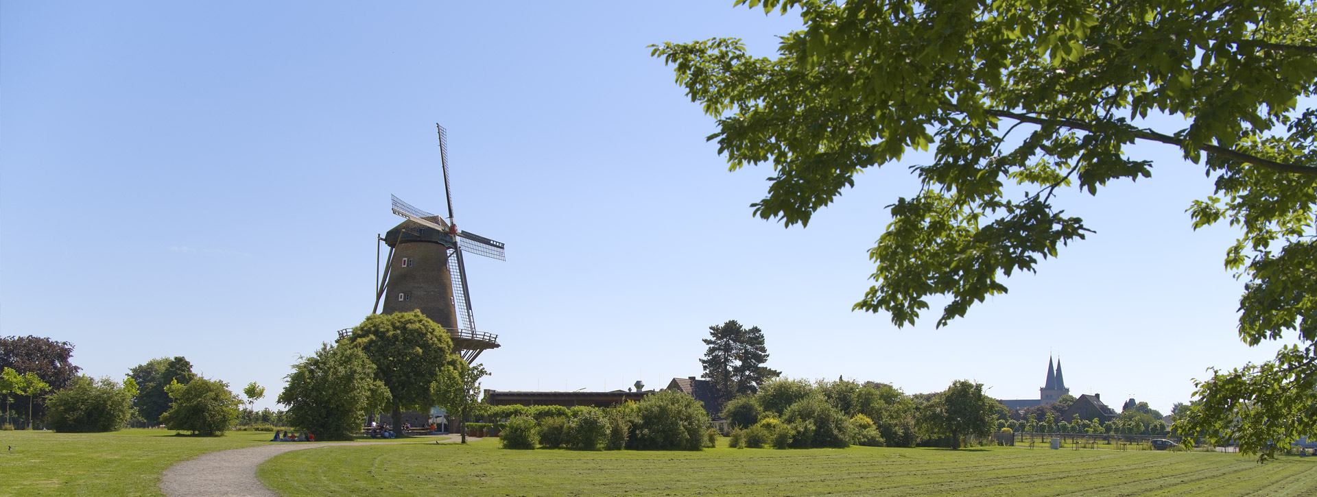 Barokke windmolen met een moderne uitbreiding aan de rechterkant, stoelen, tafels en parasols ervoor