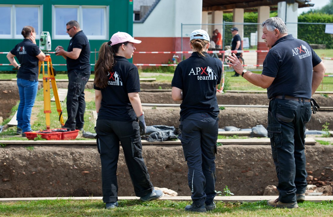 Five archaeologists from APX stand around excavation pits near the hostel