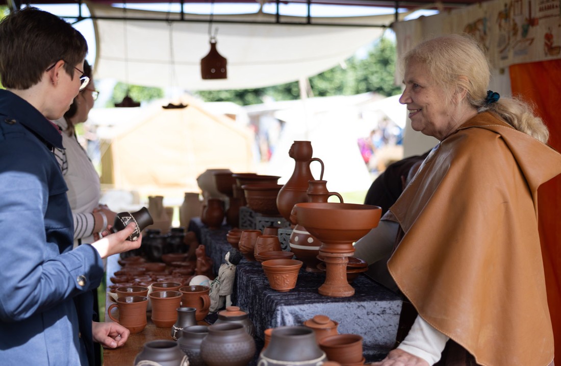 Stand mit röpmischer Töpferware, Viele Leute davor, eine lächelnde Töpferin dahinter