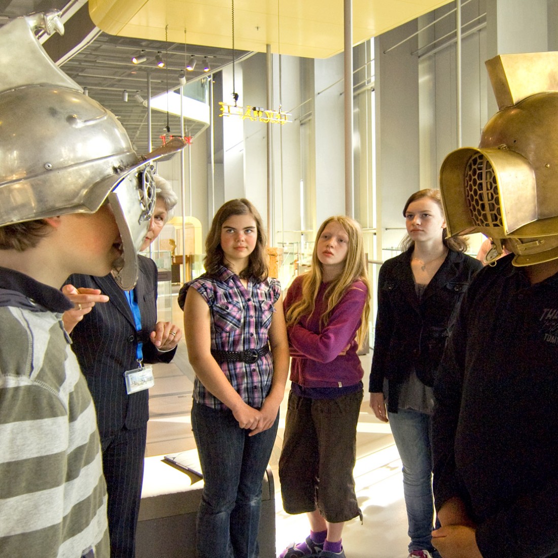 Gruppe von Schüler:innen im Museum, zwei (links und rechts) probieren Gladiatorenhelme an