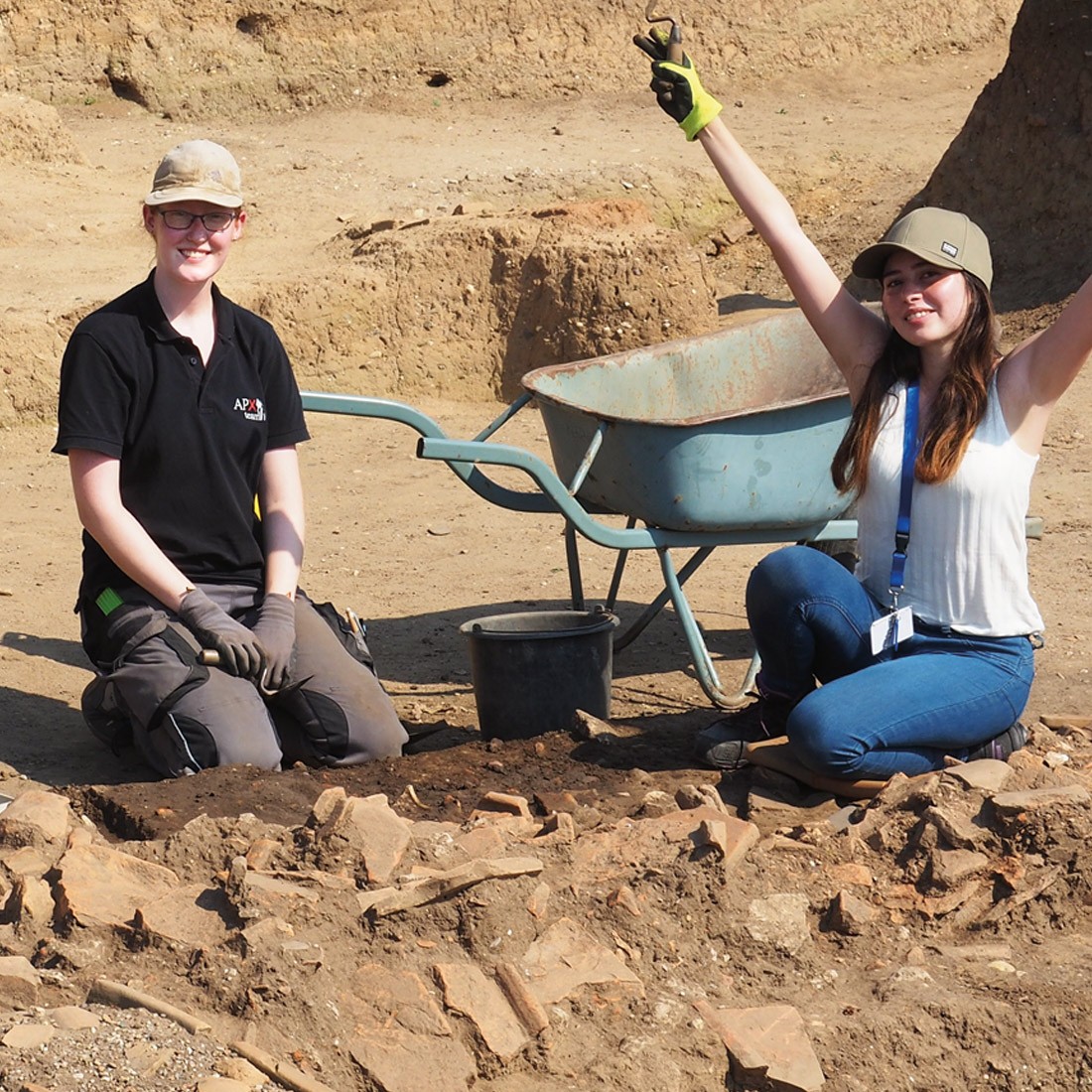 Two merry young women kneel in an archaeological dig