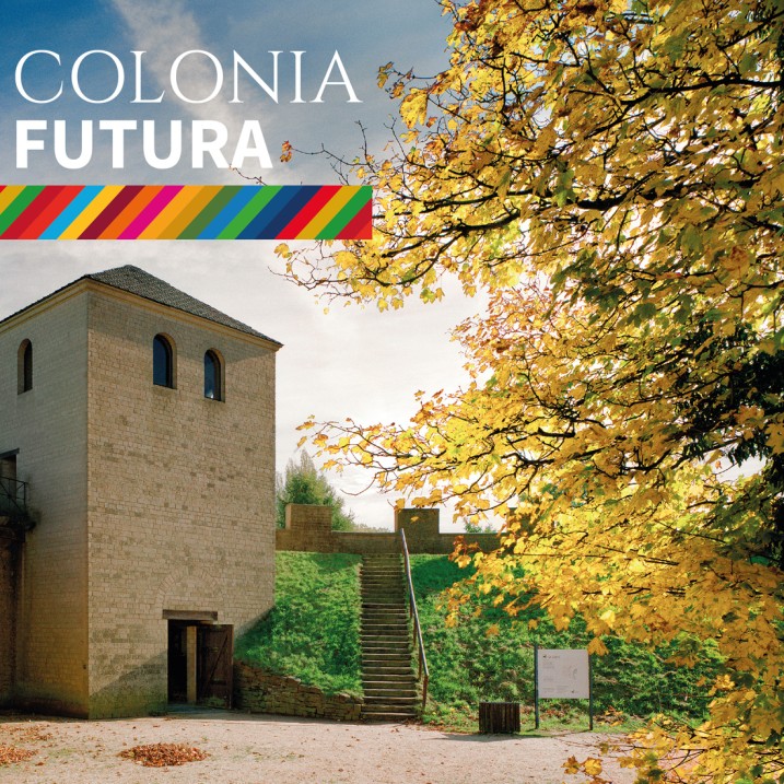 Eckturm der Stadtmauer, davor im Sonnenlicht strahlendes Herbstlaub. Schriftzug COLONIA FUTURA